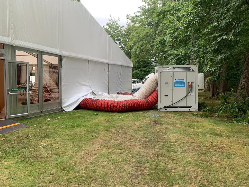 Wedding guests seated inside a large marquee kept cool with temporary air conditioning and ventilation fans