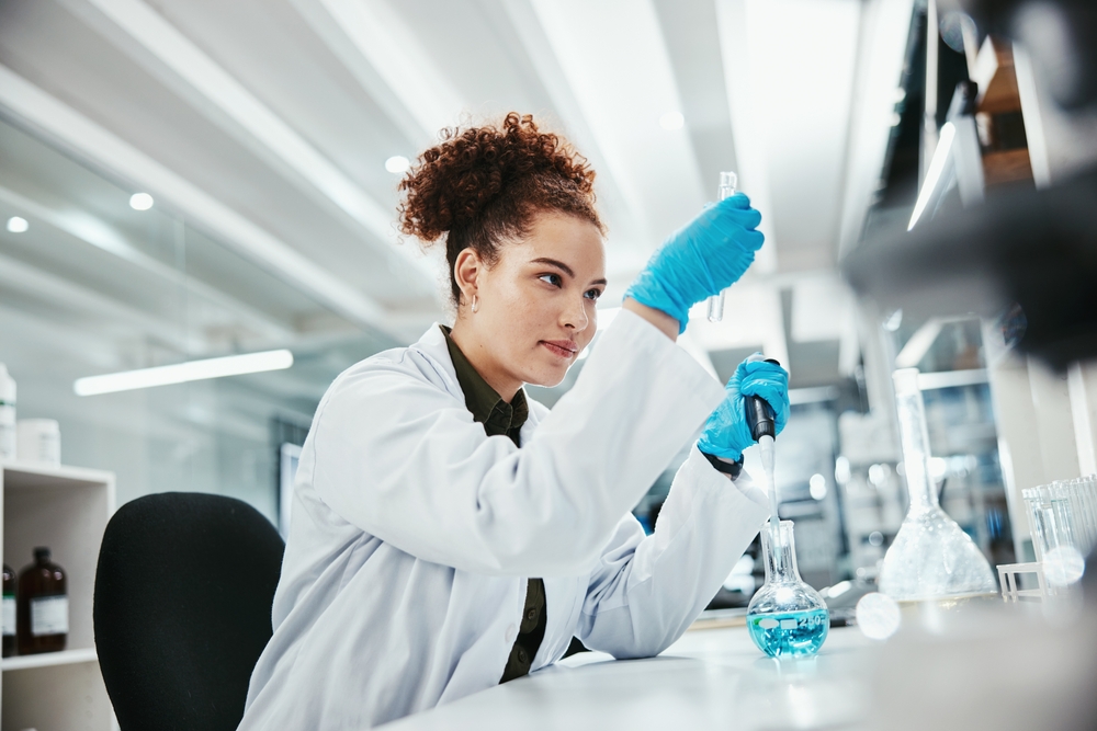 Female scientist working in a laboratory, using a pipette to transfer liquid into a flask, representing precision and innovation in pharmaceutical and industrial research.